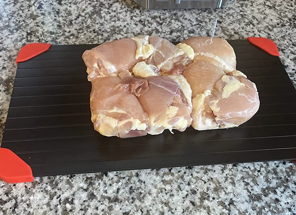 Chicken thighs thawing on a black defrosting tray