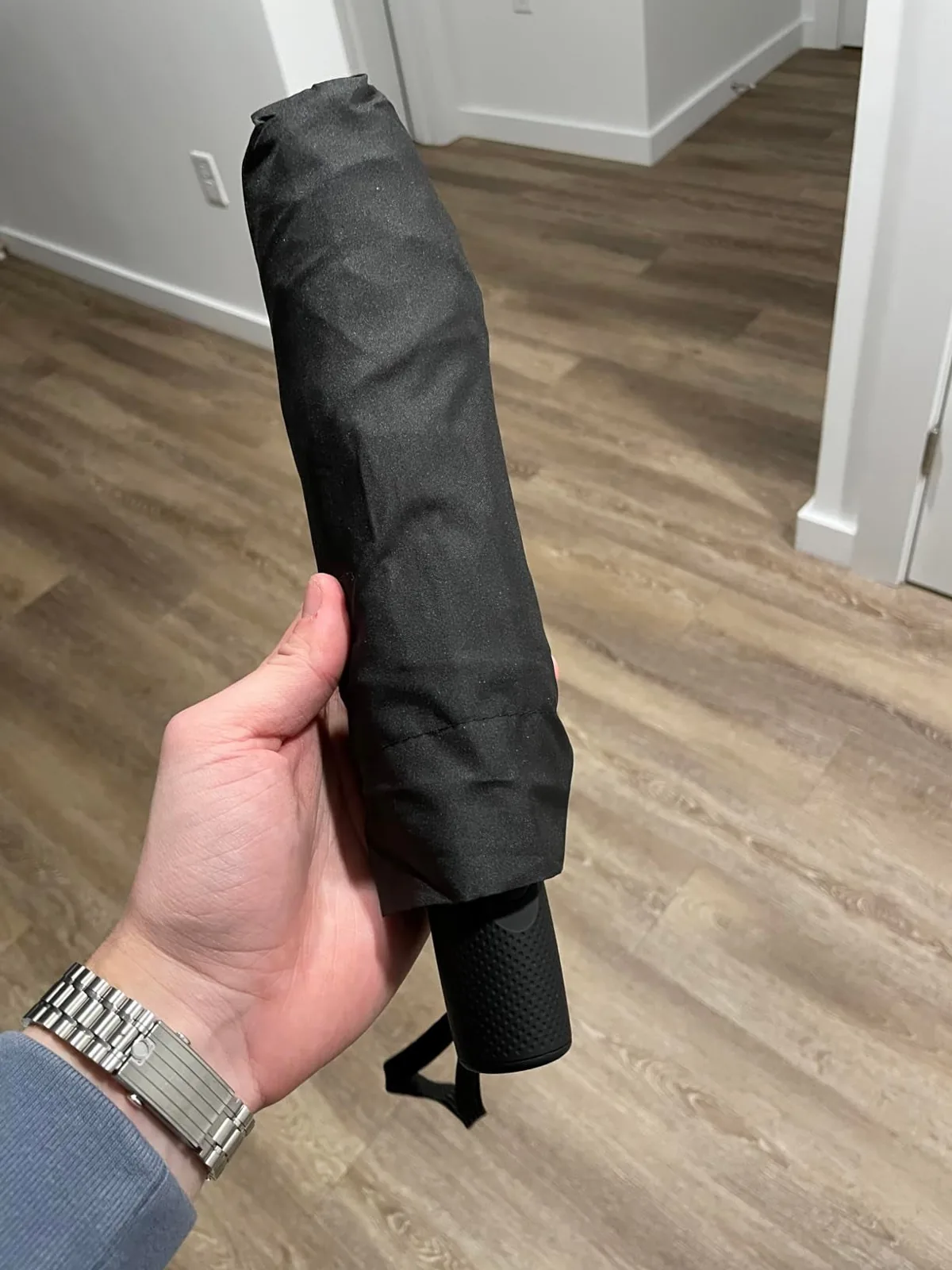 Hand holding a compact folded black Repel travel umbrella