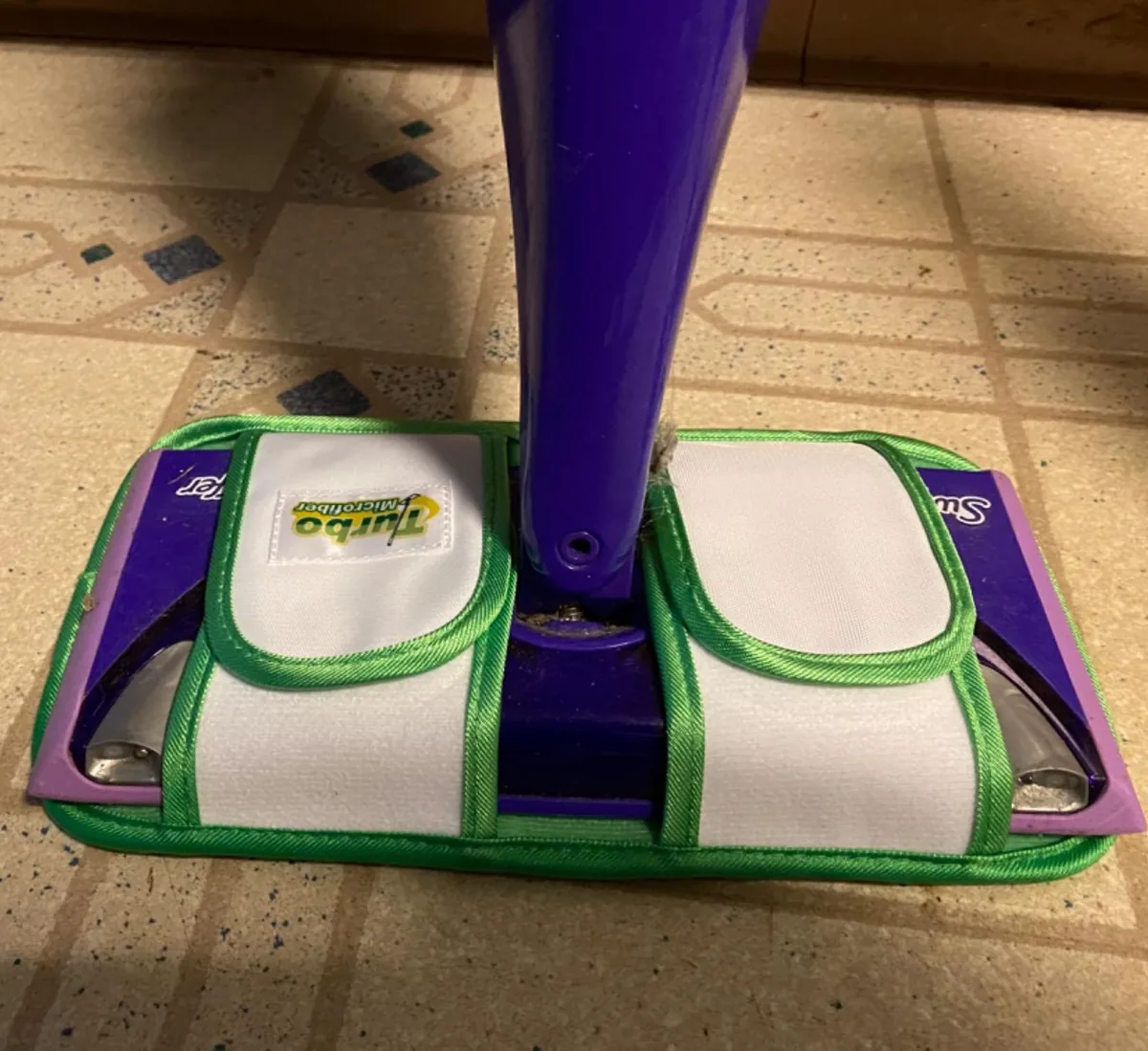 White and green reusable microfiber pad fitted on a Swiffer mop over a tile floor