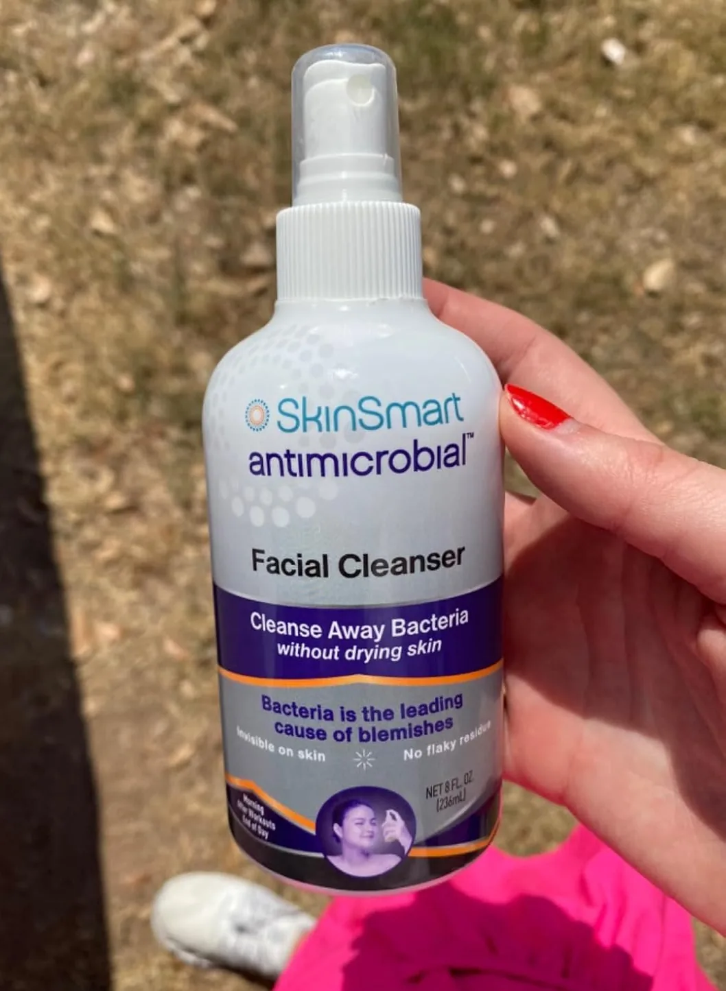 Hand holding a bottle of SkinSmart antimicrobial facial cleanser spray outdoors