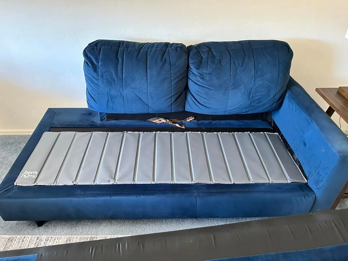 Fabric-covered slatted support board laid across a sofa seat under the cushions