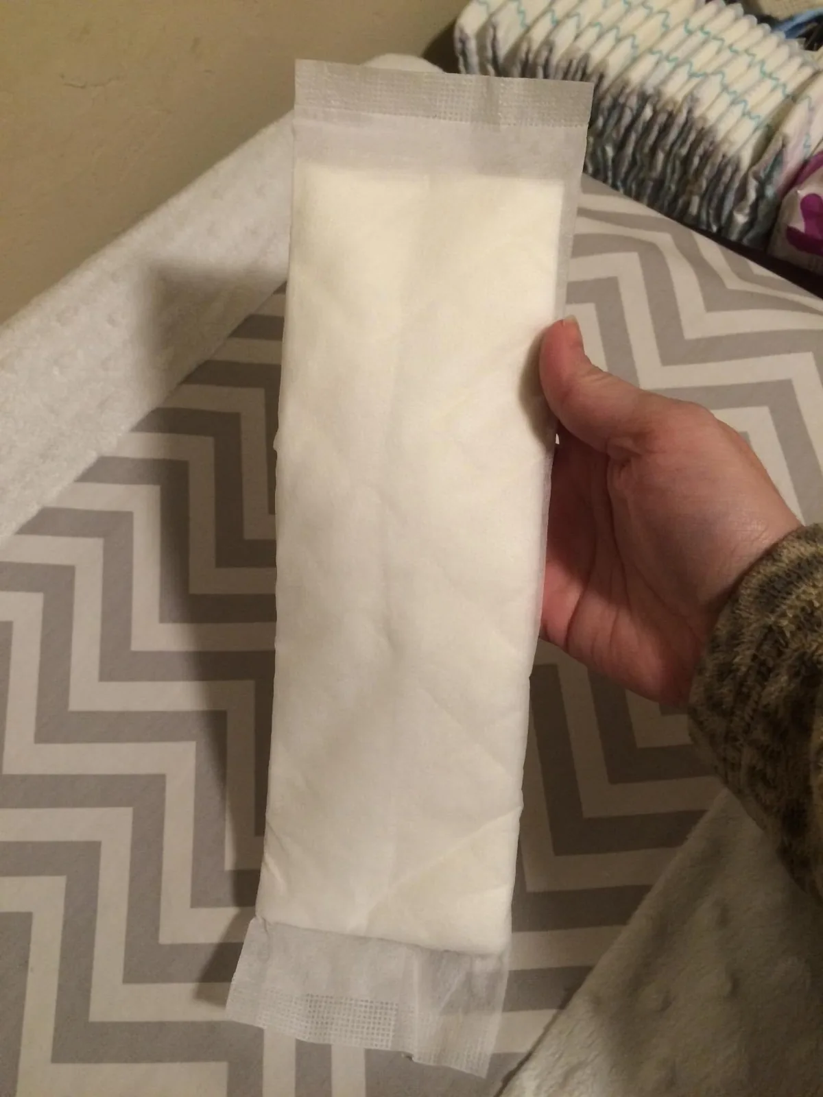 Hand holding a large absorbent diaper booster pad above a stack of diapers