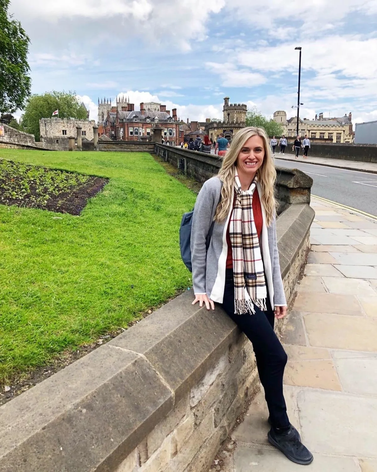 Woman wearing a cream and red tartan plaid scarf with a grey cardigan on a city street
