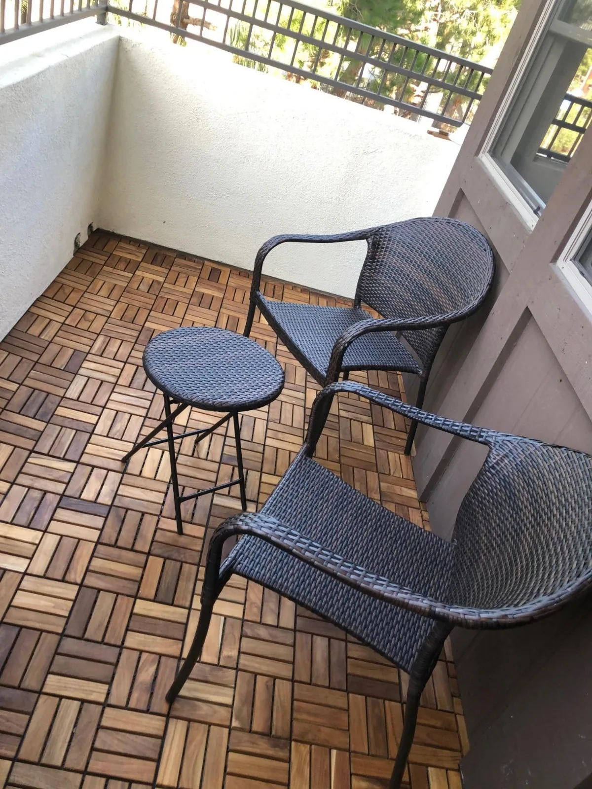 Wicker chairs and a small table on a balcony floored with teak interlocking tiles