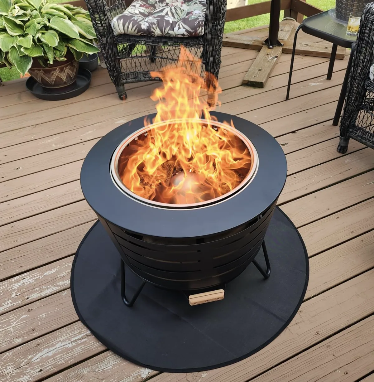 Black TIKI smokeless fire pit burning on a wooden deck beside patio chairs