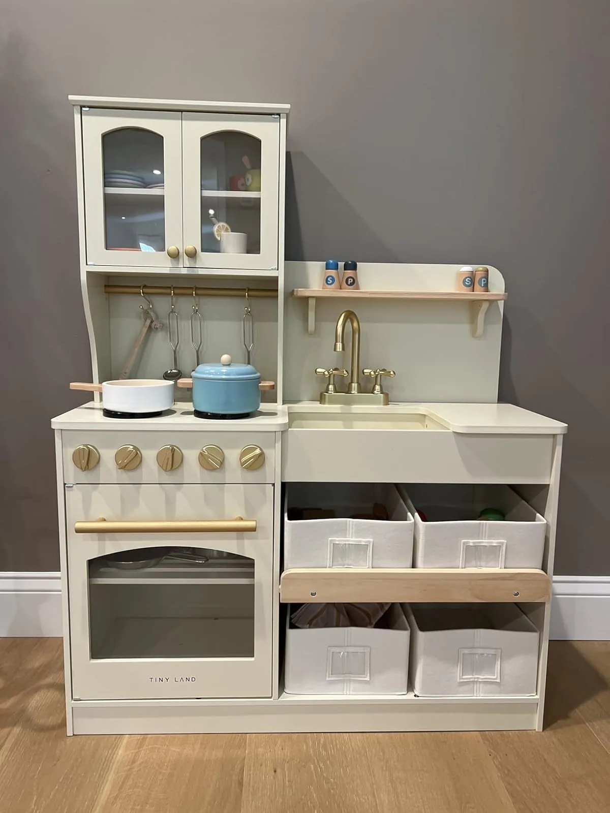 Cream wooden play kitchen with stove, oven, sink, hanging utensils and storage bins
