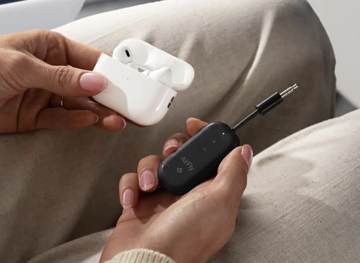 Hands holding a Twelve South AirFly Pro Bluetooth transmitter and a case of wireless earbuds