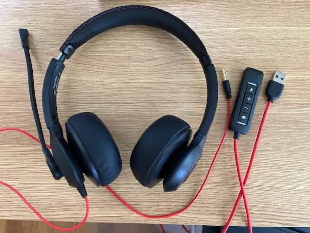 Black USB headset with a boom mic, red cable and inline control pod on a wooden desk