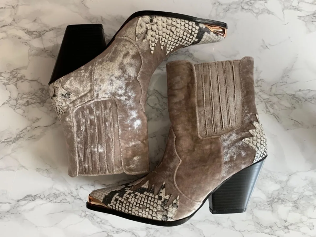 Pair of velvet and snakeskin-print western ankle booties on a marble surface