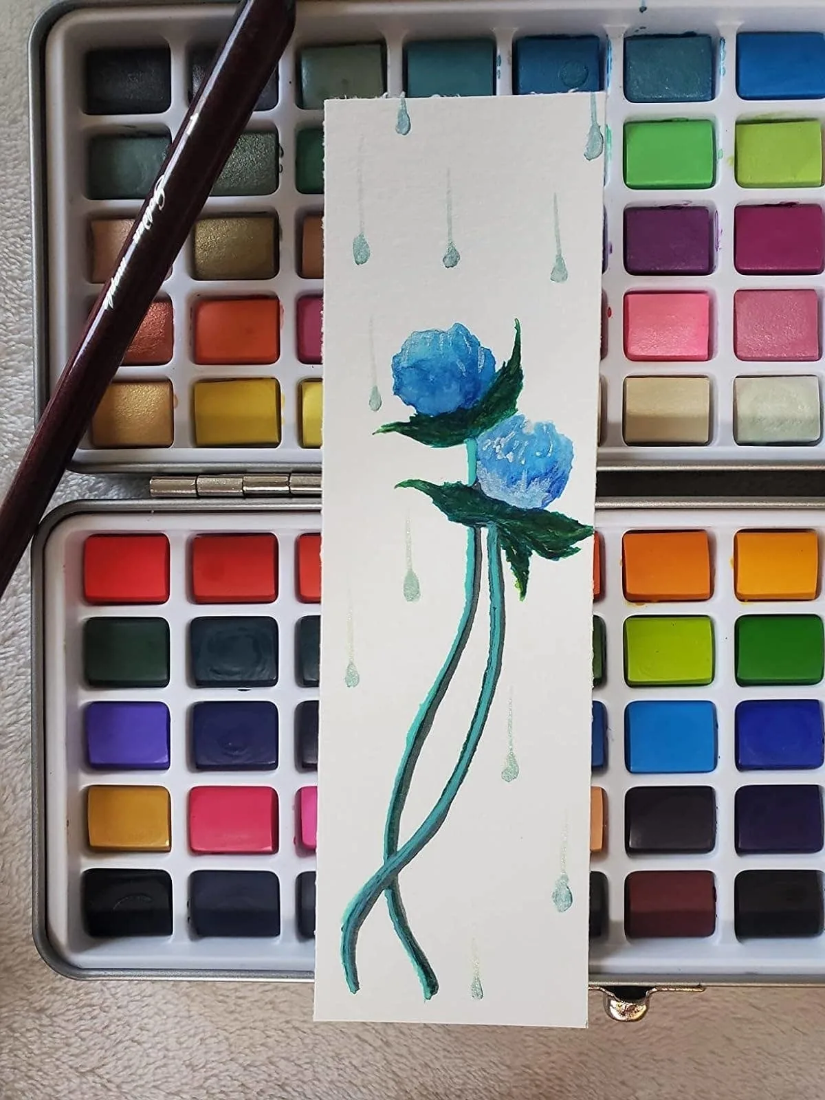 Watercolor floral painting resting on a metal watercolor palette tin