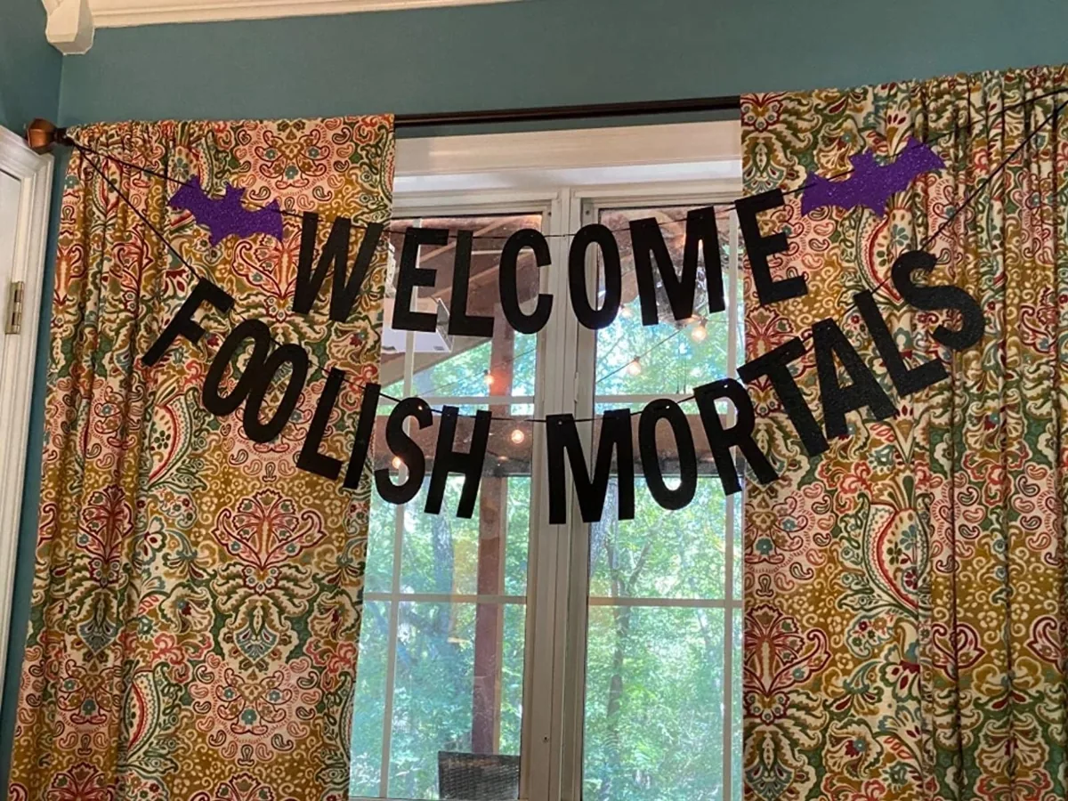 Black glitter Welcome Foolish Mortals banner with bats hanging in a window