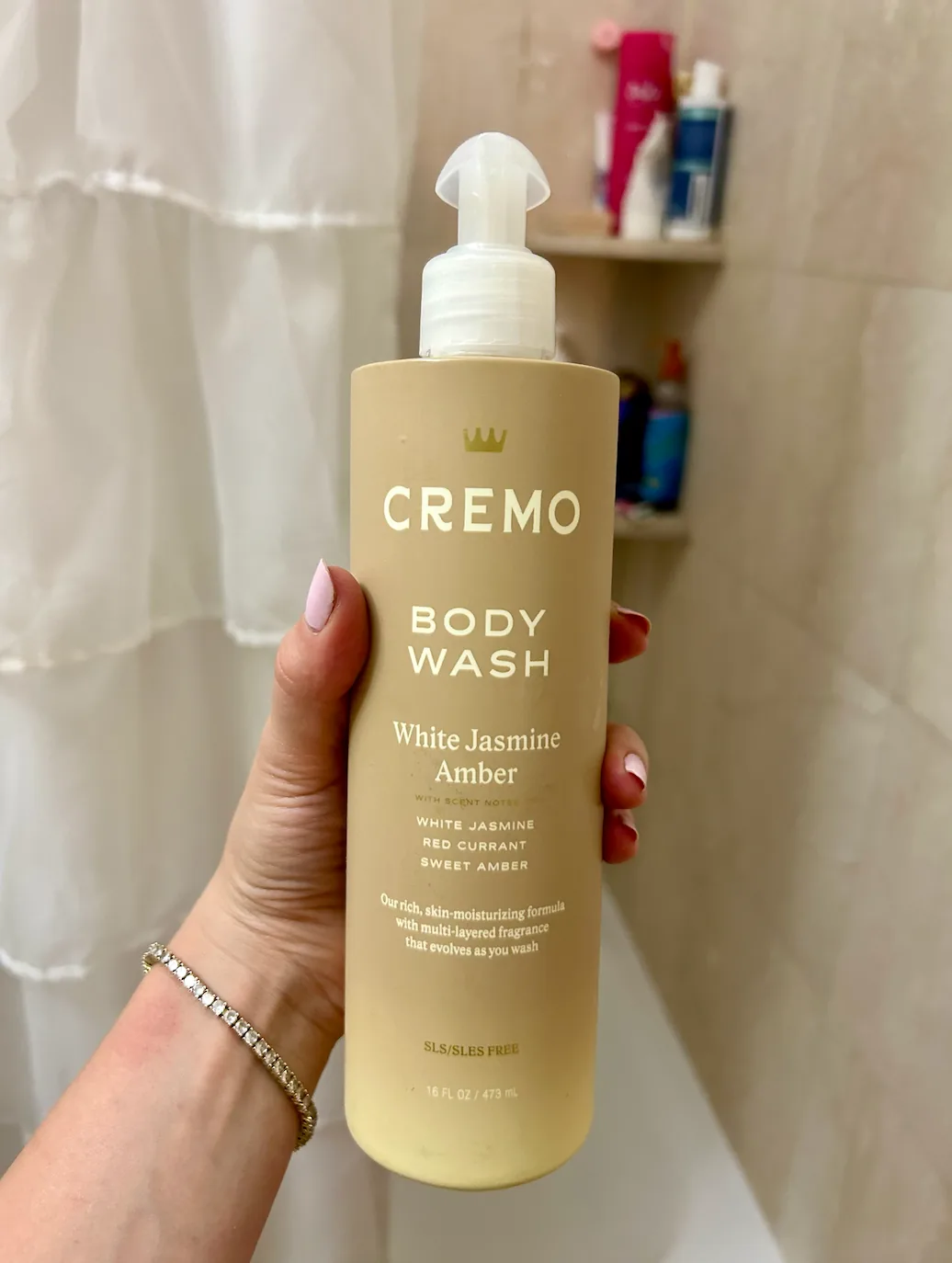 Hand holding a bottle of white jasmine amber body wash in a shower
