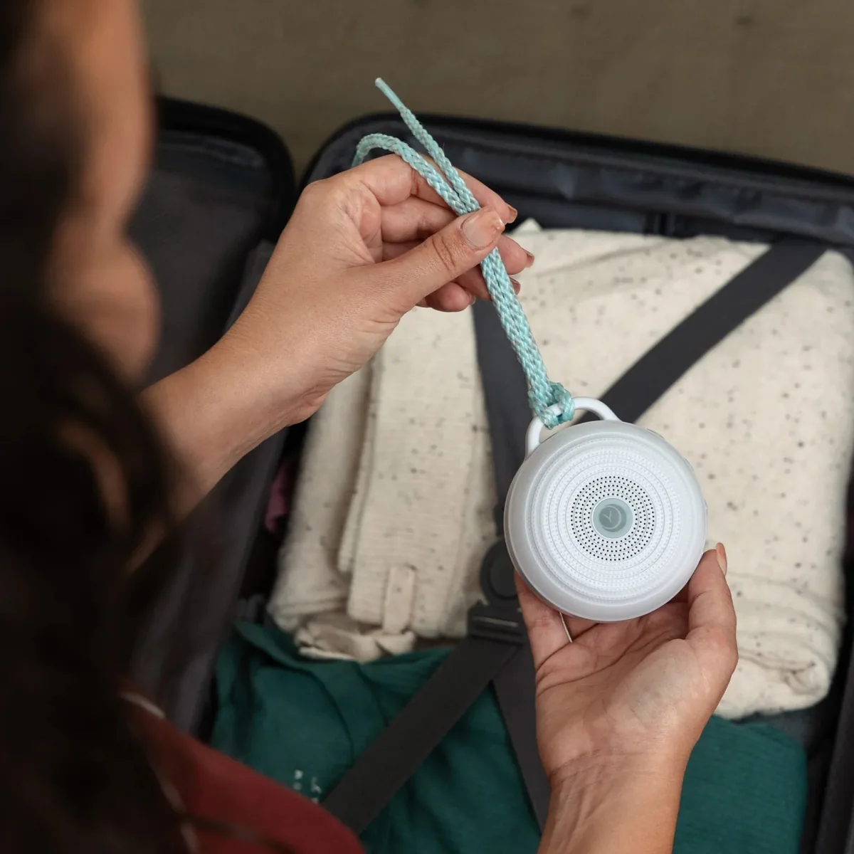 Yogasleep Rohm portable white noise machine held over an open suitcase